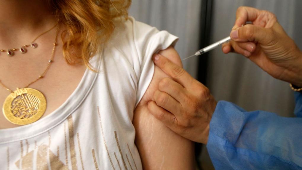 Mão aplicando vacina em braço de mulher jovem