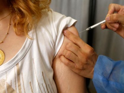Mão aplicando vacina em braço de mulher jovem