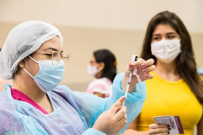 Enfermeira usando óculos e equipamentos de proteção individual manipulando seringa com vacina contra Covid-19