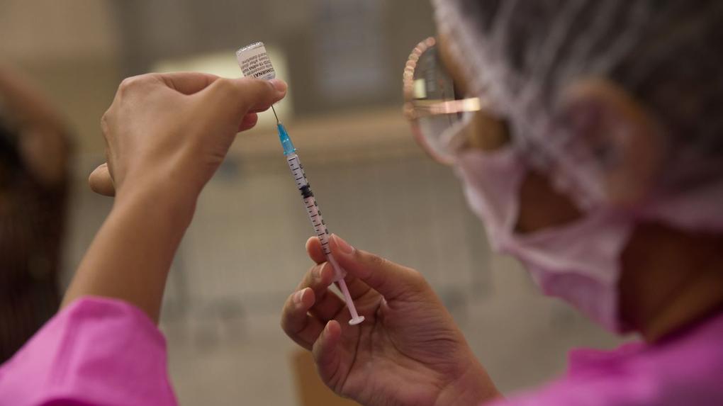 profissional de saúde vestindo jaleco rosa coloca dose de vacina em seringa