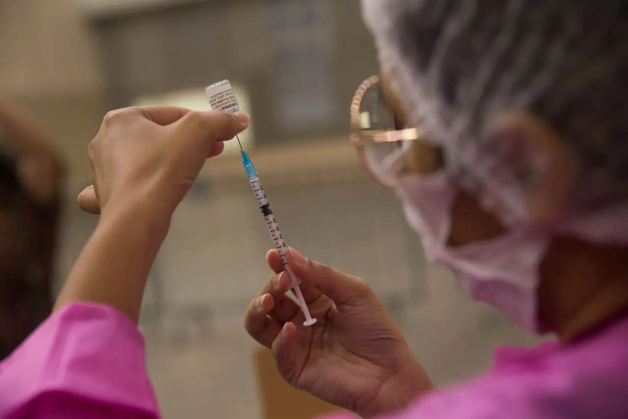 profissional de saúde vestindo jaleco rosa coloca dose de vacina em seringa