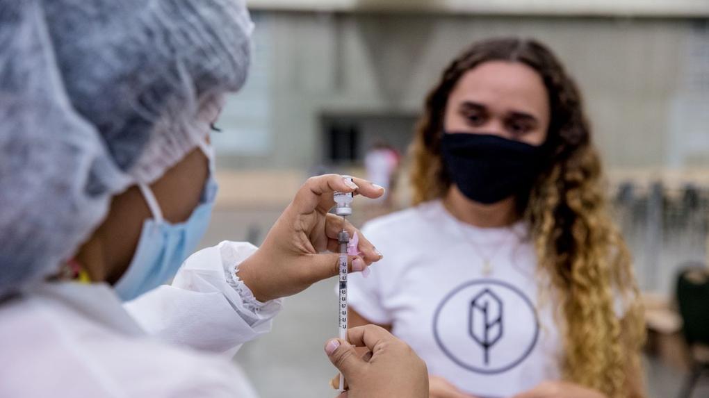 profissional de saúde injeta dose de vacina em seringa enquanto jovem observa