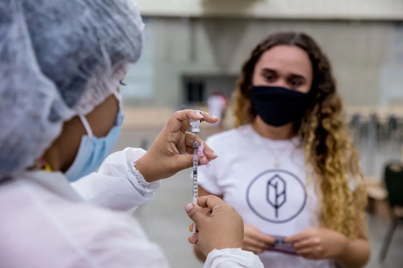 profissional de saúde injeta dose de vacina em seringa enquanto jovem observa