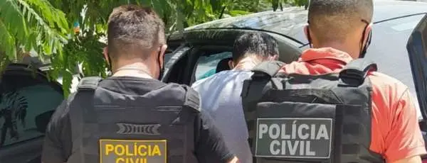 Imagem mostra dois policiais civis com fardas da instituição prendendo um homem