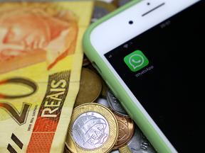 Celular, com o aplicativo Whatsapp aberto na tela, em cima de cédulas de dinheiro brasileiro