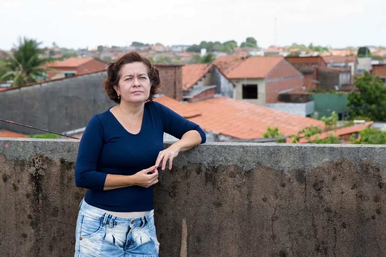 mulher encostada em muro com casas ao fundo