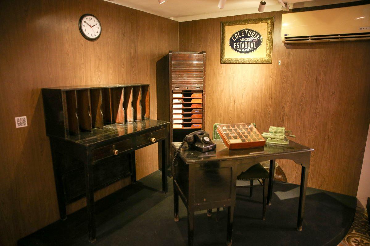 Sala de exposição histórica do Centro de Memória da Sefaz, com mesas, arquivos e telefone antigo