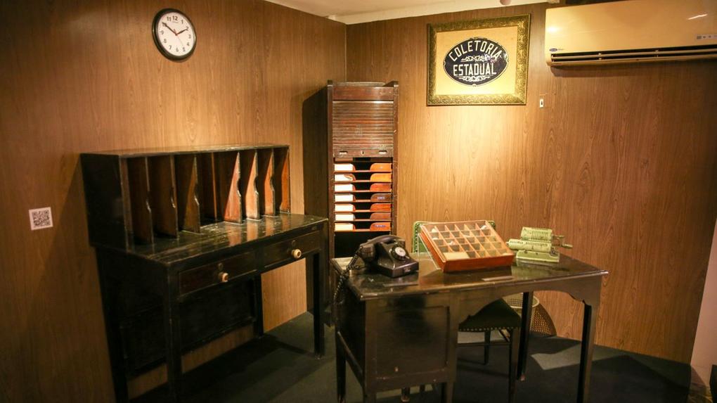 Sala de exposição histórica do Centro de Memória da Sefaz, com mesas, arquivos e telefone antigo