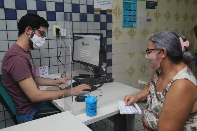 Mulher sendo atendida por funcionário do Cras em Fortaleza. Os dois estão sentados e usando máscaras de proteção facial