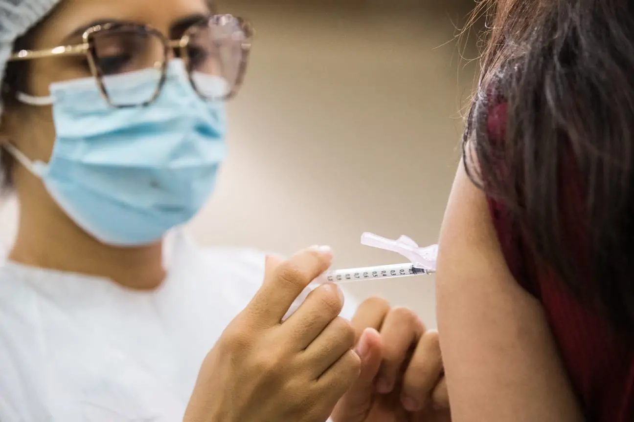 Profissional da saúde aplicando vacina contra a Covid-19 em uma mulher