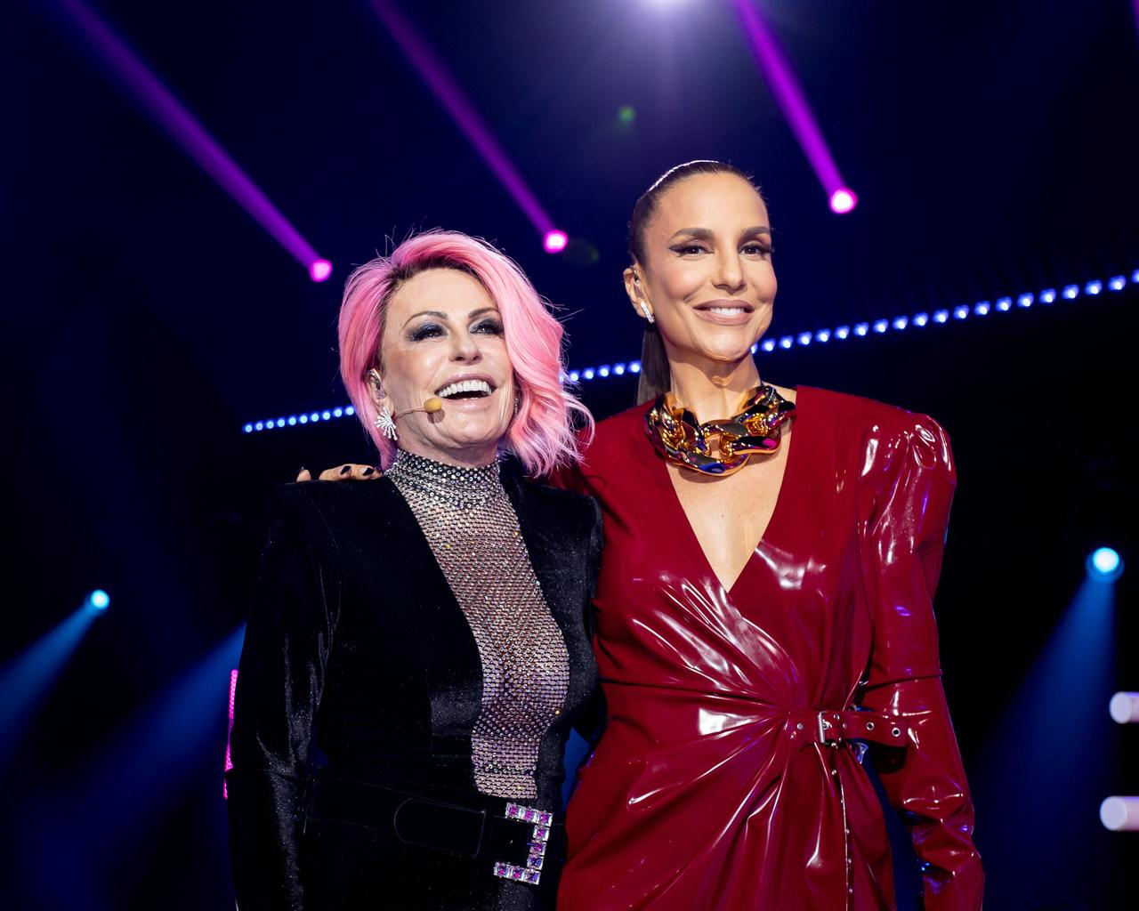 Ana Maria Braga sorridente ao lado de Ivete Sangalo, de vestido vermelho