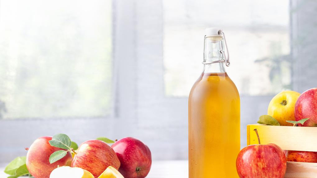 Maças ao lado de um garrafa com vinagre de maçã