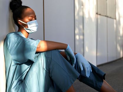 Profissional de saúde negra sentada em chão de hospital cansada, possivelmente com síndrome de Burnout
