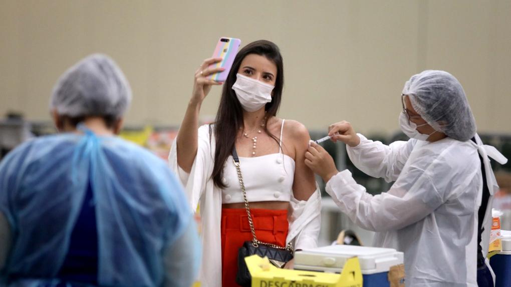 Mulher tira selfie enquanto é vacinada contra a Covid-19 por profissional de saúde em Fortaleza, no Ceará