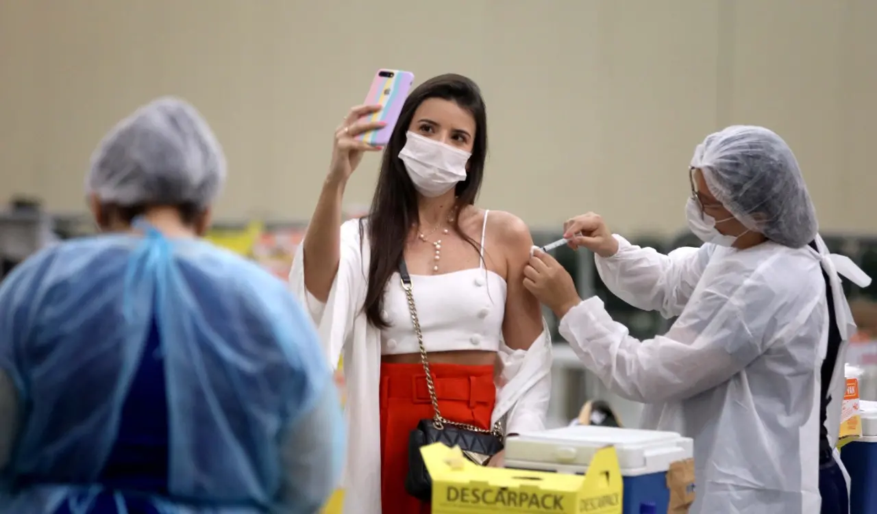 Mulher tira selfie enquanto é vacinada contra a Covid-19 por profissional de saúde em Fortaleza, no Ceará