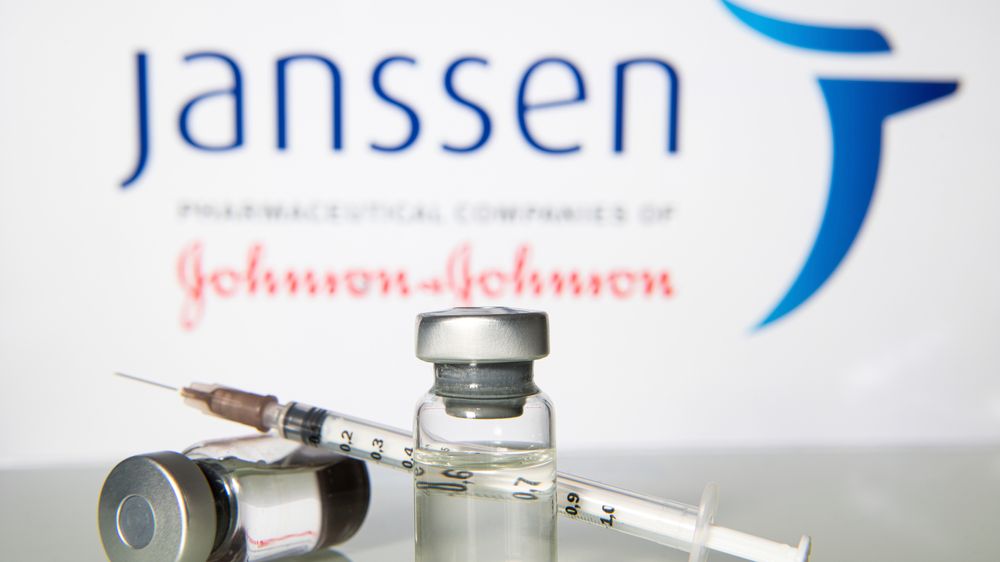 A imagem mostra frascos com a vacina Janssen em frente à logo da farmacêutica Johnson & Johnson.