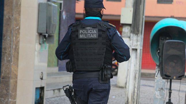 Policial militar está de costas, caminhando por uma comunidade.