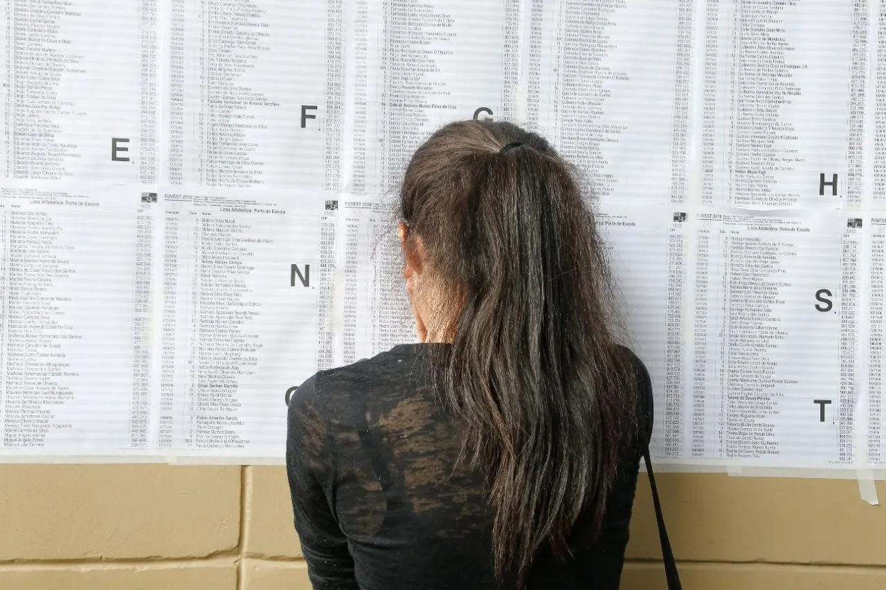 mulher de costas diante de lista de aprovados do vestibular da Fuvest