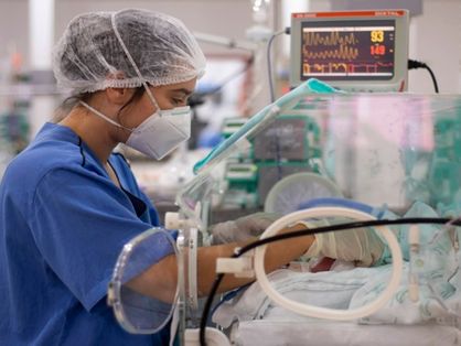 Profissional da saúde com máscara, touca e bata azul em uma UTI neonatal