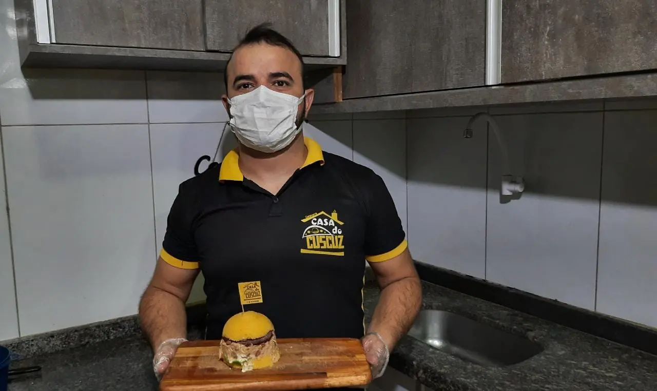 Empresário Francisco José, o Fran, segura a tábua onde está posicionado um dos seus hambúrgueres de cuscuz