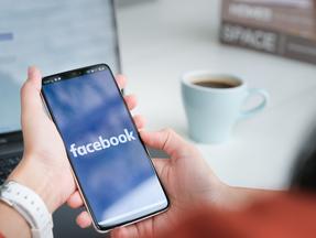 Mão segura celular ligado aparecendo a logo do Facebook na tela