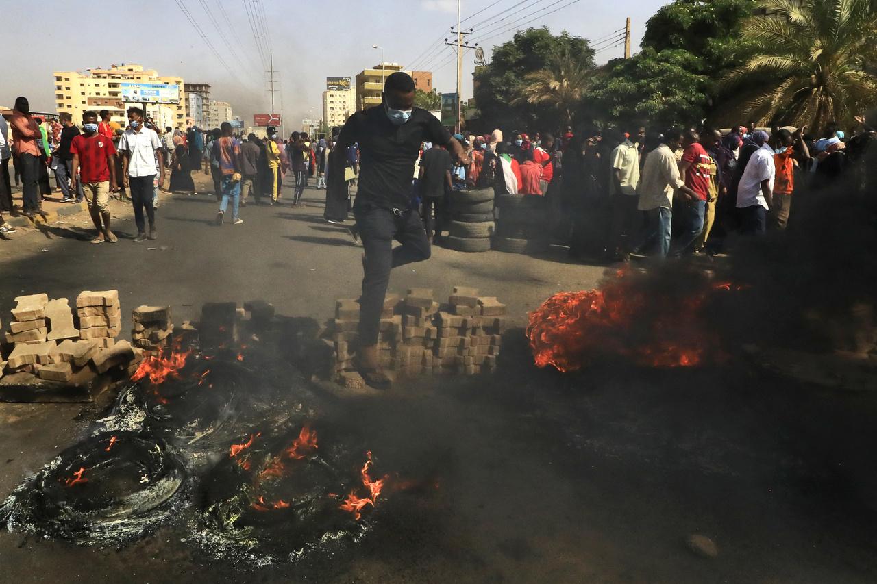 Manifestantes sudaneses saltam sobre um bloqueio de estrada feito de tijolos e pneus em chamas enquanto se manifestam na 60th Street na capital Cartum