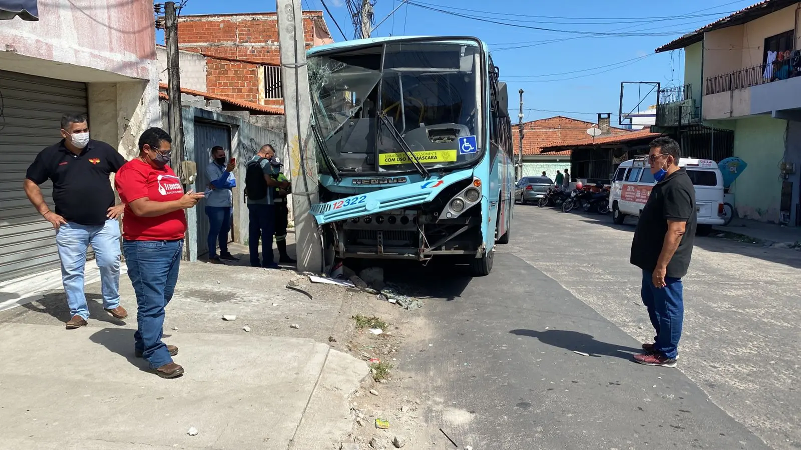 Ônibus com a dianteira direita avariada junto ao poste. Pessoas no local da ocorrência