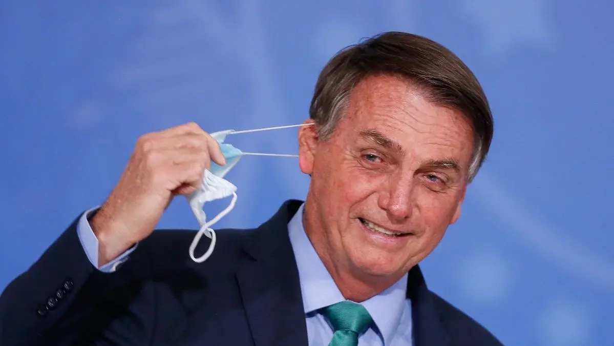 Imagem mostra o presidente Jair Bolsonaro retirando a máscara de proteção contra a Covid-19.