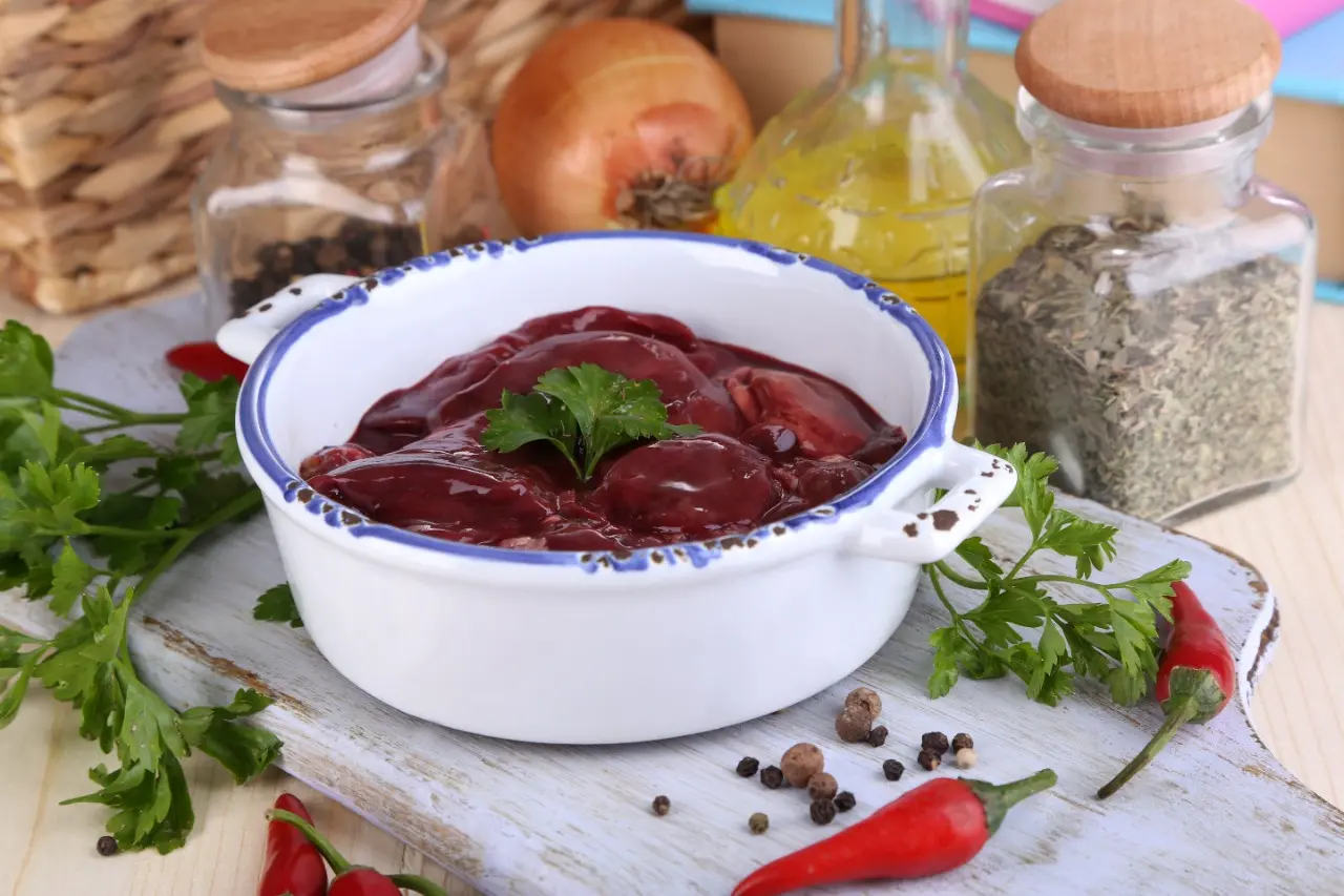 Fígado animal disposto em um panela sobre uma mesa ao lado de especiarias e temperos