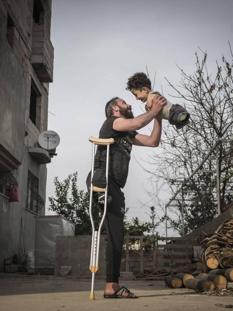 Foto do turco Mehmet Aslan mostra o pai levantando o filho para o alto, enquanto se apoia em uma muleta