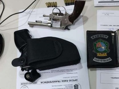 A imagem mostra uma pistola e munições dispostos sobre a mesa da delegacia.