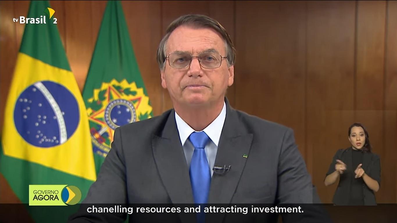 Bolsonaro de terno e gravata discursando, com uma tradutora de libras no canto da tela