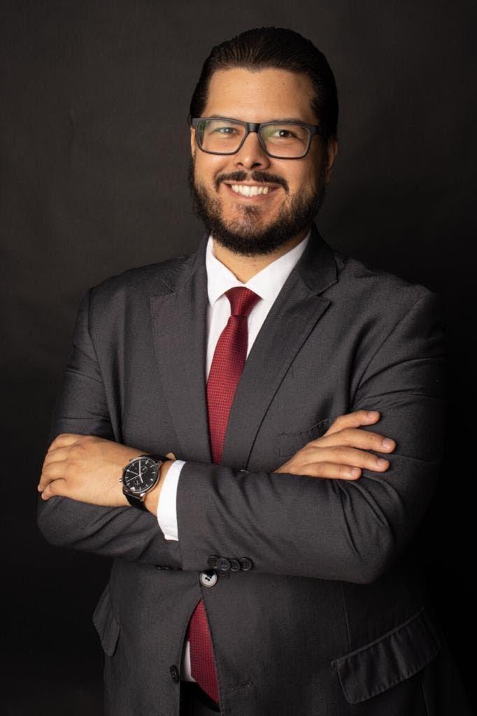 Advogado Agnaldo Bastos posa sorrindo para foto, usando terno e gravata
