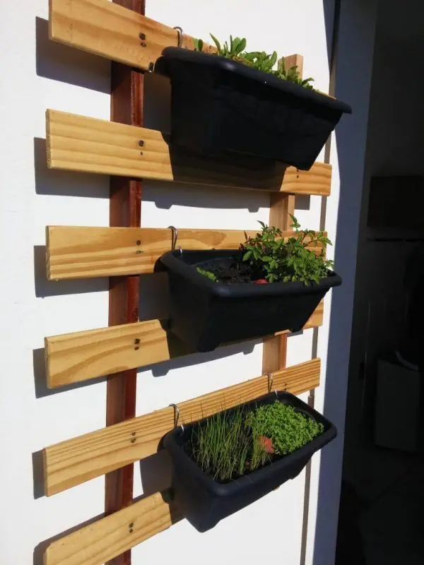 A imagem mostra uma horta suspensa com três vasos pretos.