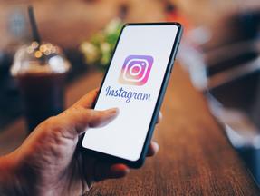 Mão segurando um celular, com a tela mostrando a logo do Instagram