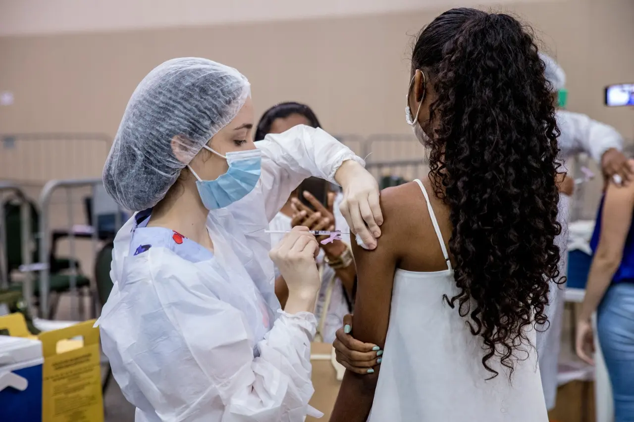 Uma mulher aplica a vacina contra a Covid-19 numa adolescente.