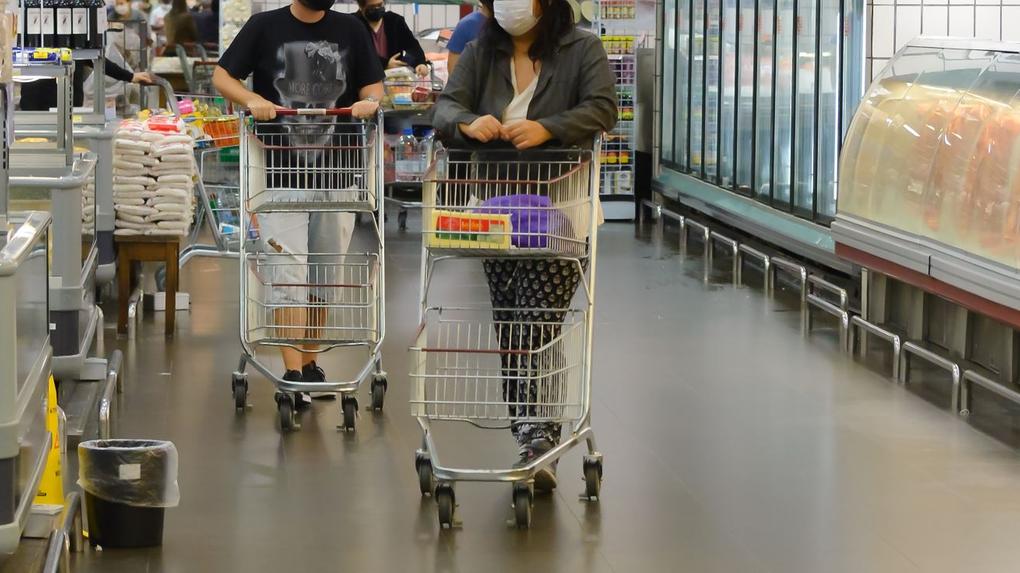Pessoas andando em supermercado com carrinhos de compras quase vazios