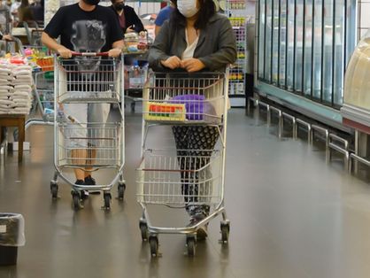 Pessoas andando em supermercado com carrinhos de compras quase vazios