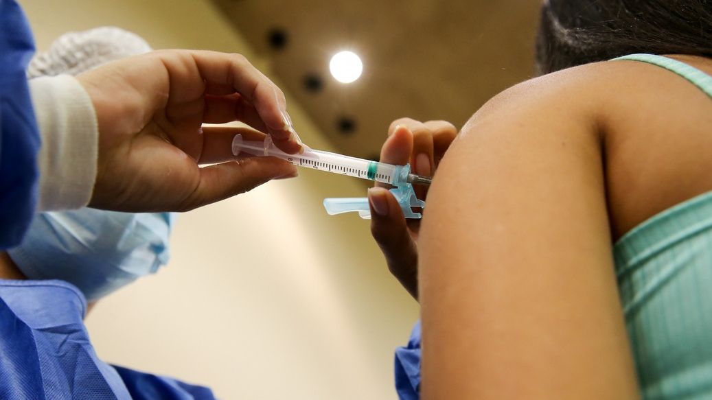 Enfermeiro aplica vacina contra a Covid-19 no braço de uma mulher.