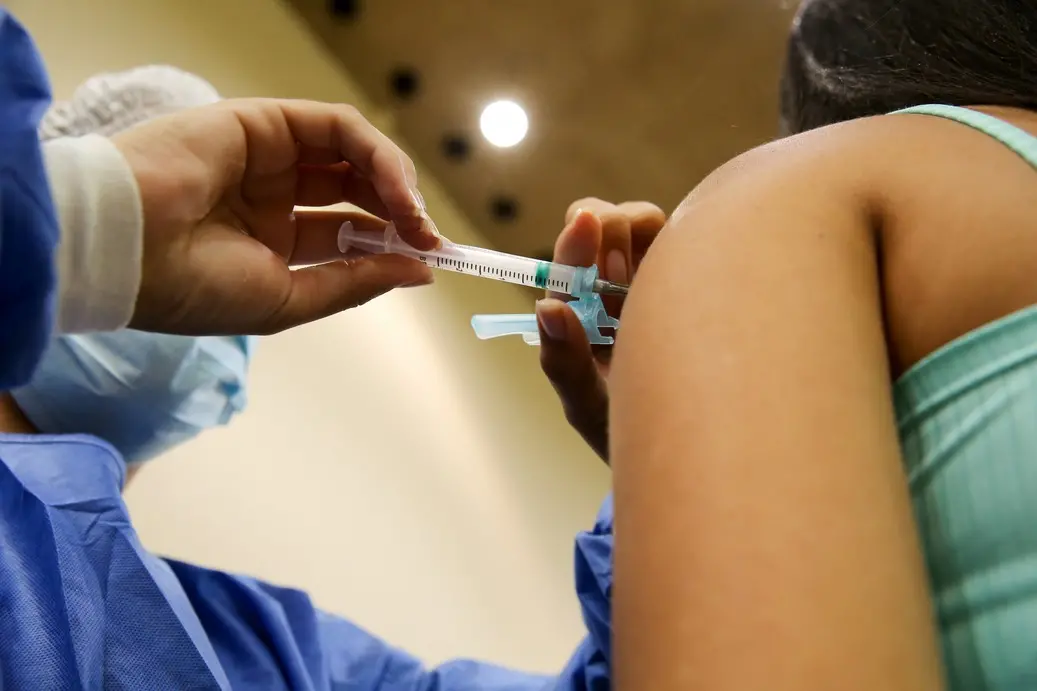 Enfermeiro aplica vacina contra a Covid-19 no braço de uma mulher.
