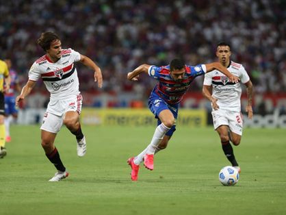 Bruno Melo tropeça com a bola observado por jogador do São Paulo