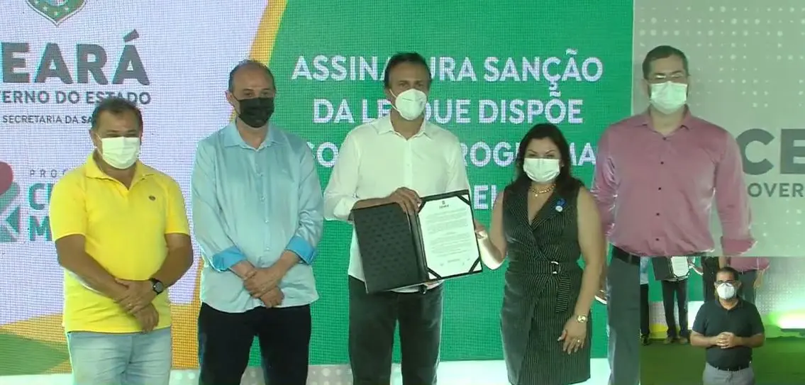 Governador Camilo Santana (PT) segurando documento da lei entre o secretário Estadual da Saúde (Sesa), Marcos Gadelha; o vice-presidente do Conselho Estadual de Saúde (Cesau), Francisco Adriano Fernandes; a presidente do Conselho de Secretários Municipais de Saúde do Ceará (Cosems), Sayonara Moura; e o coordenador do programa Cuida Melhor, Caio Cavalcante.