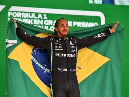 Lewis hamilton no pódio da F! segurando a bandeira do Brasil