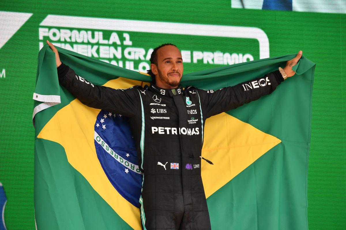 Lewis hamilton no pódio da F! segurando a bandeira do Brasil