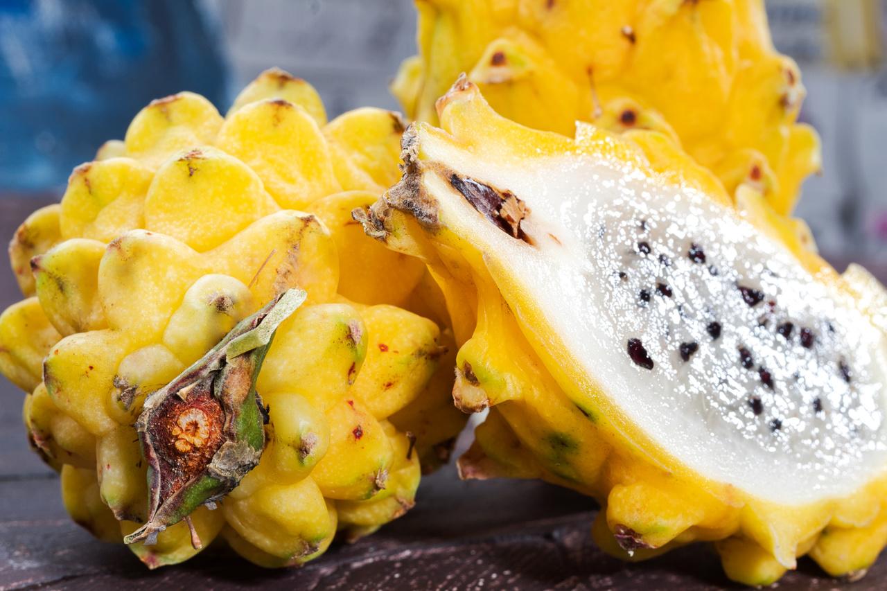 Frutos de pitaya amarela inteiros e um partido ao meio sobre um fundo amadeirado