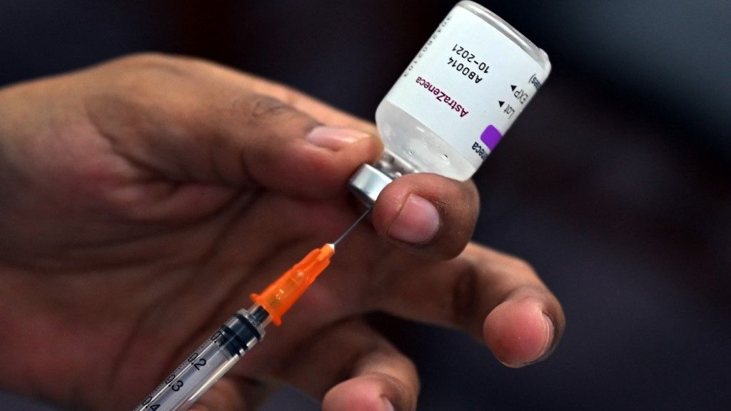 Mão segurando seringa retirando conteúdo de frasco de vacina da AstraZeneca
