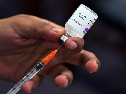 Mão segurando seringa retirando conteúdo de frasco de vacina da AstraZeneca