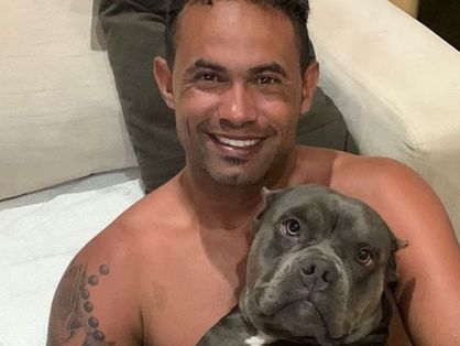 O goleiro Bruno Fernandes posa ao lado de uma cadela preta da raça pitbull.