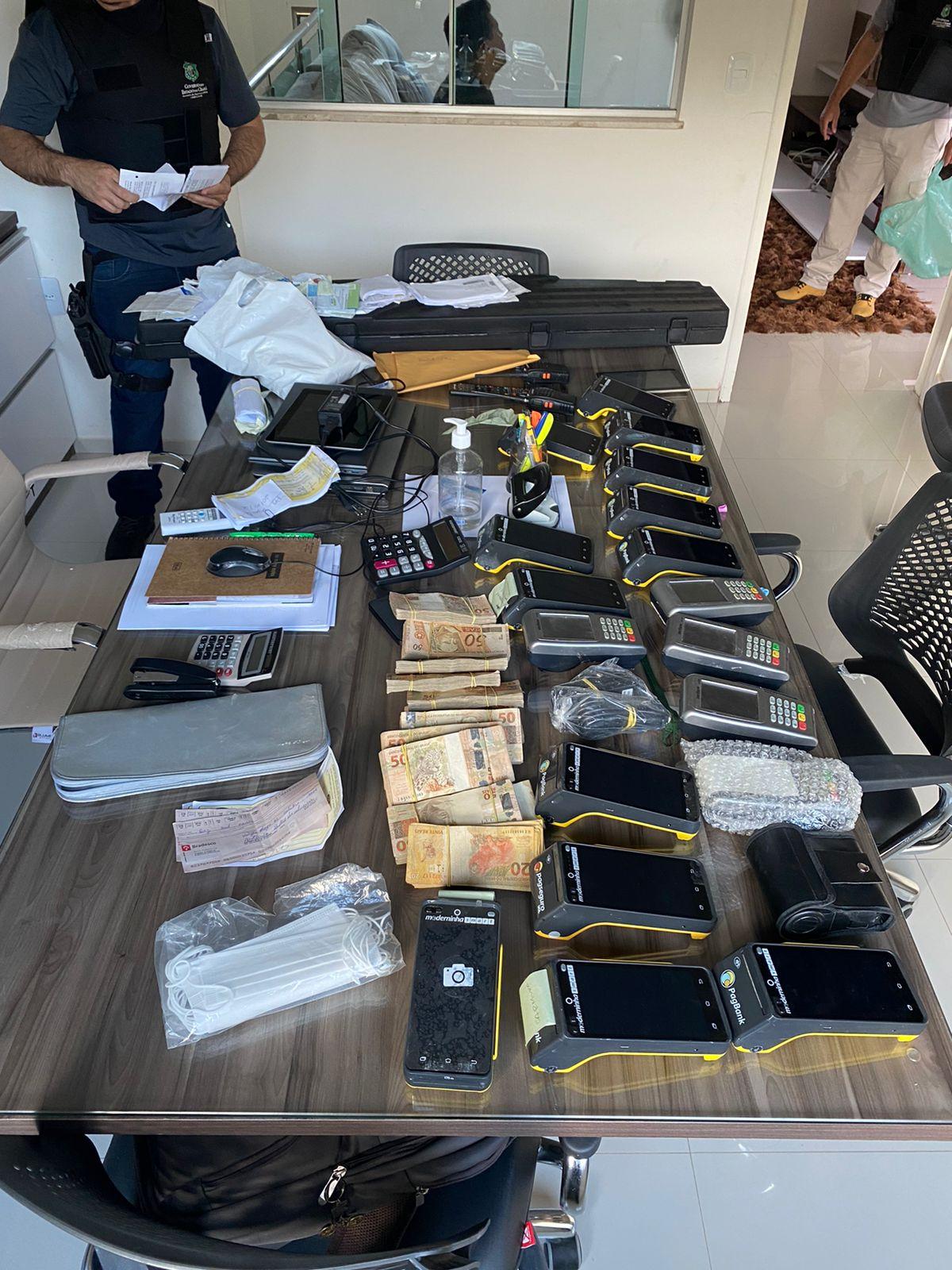 Itens apreendidos. Dentre eles, celulares, maquinetas de cartão e dinheiro