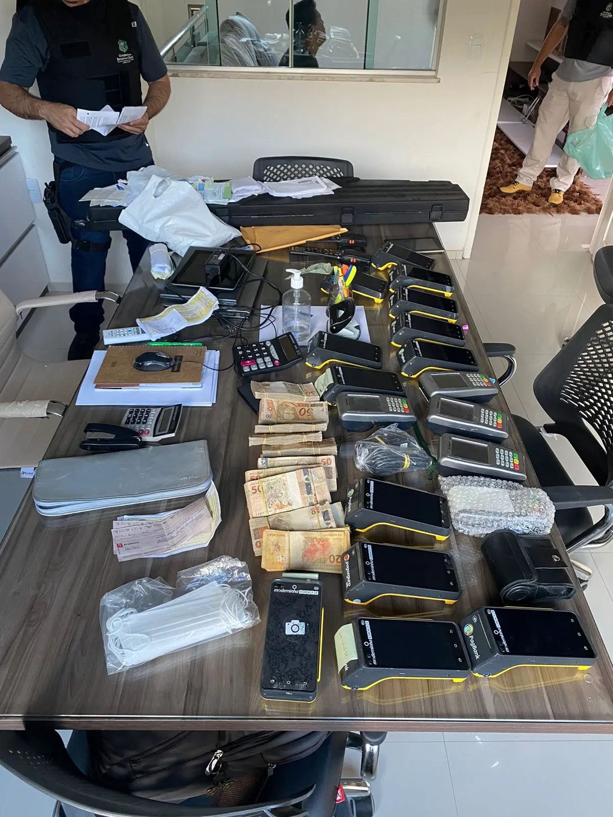 Itens apreendidos. Dentre eles, celulares, maquinetas de cartão e dinheiro